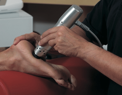 Close-up of a patient receiving a radial shockwave therapy massage on their foot at a holistic clinic.